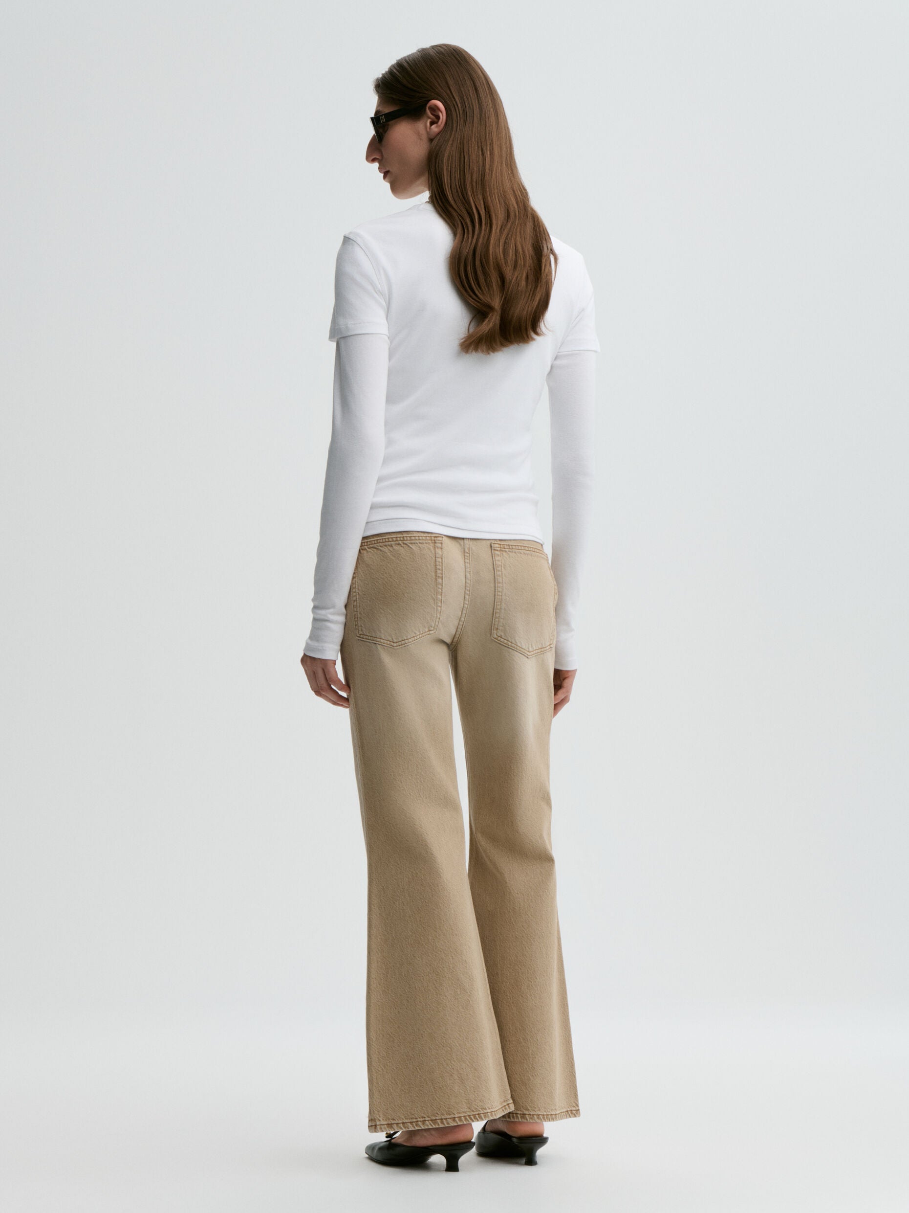 Woman wearing a white long-sleeve top and beige flared pants on a white background