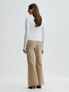 Woman wearing a white long-sleeve top and beige flared pants on a white background
