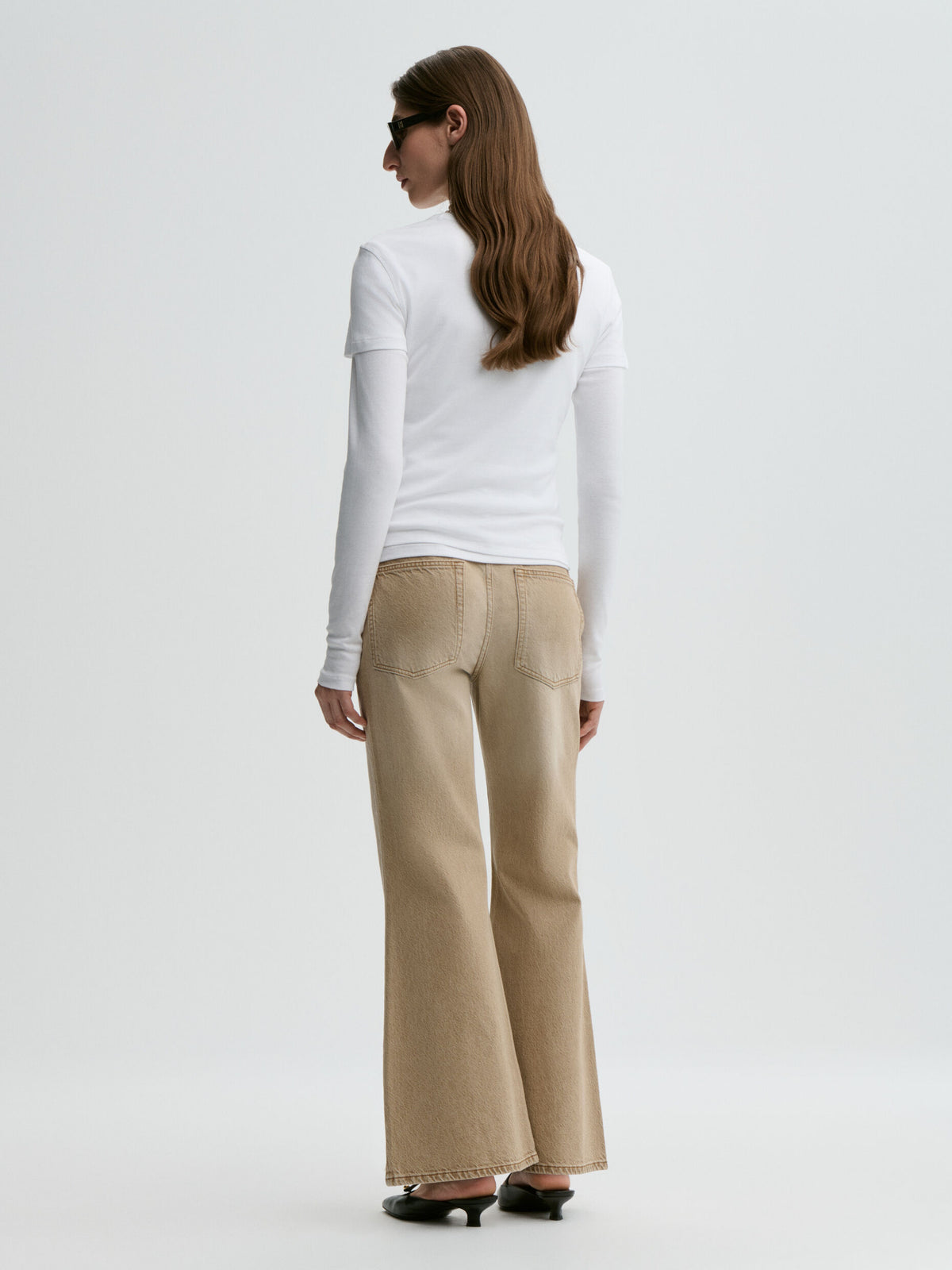 Woman wearing a white long-sleeve top and beige flared pants on a white background