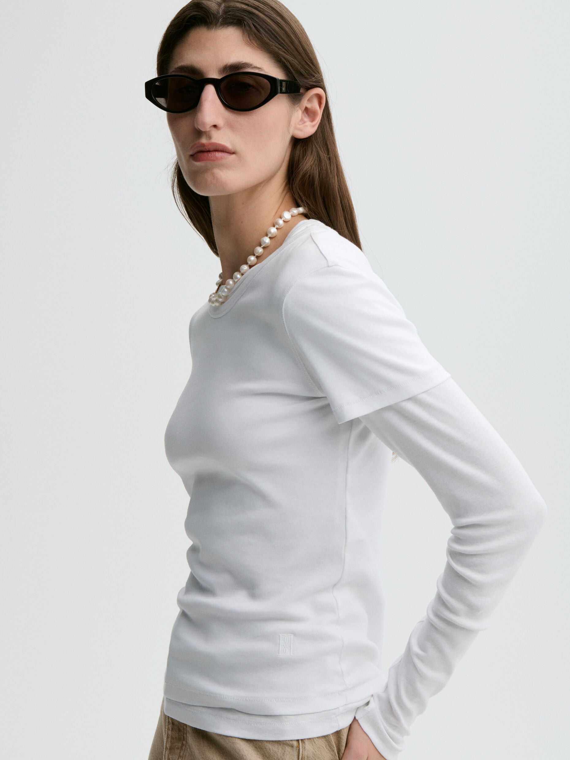 Woman wearing a white long-sleeve top and sunglasses on a light gray background