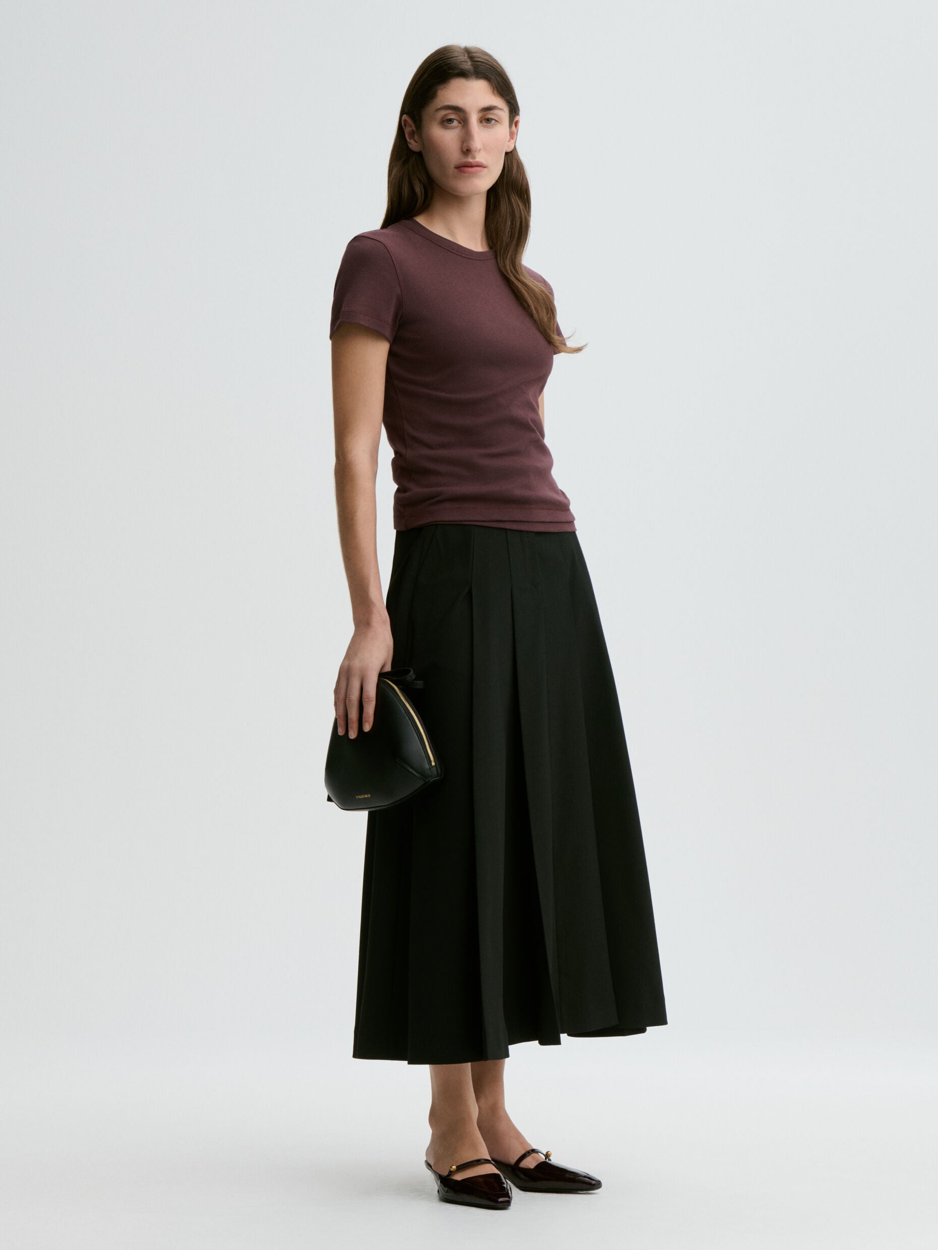 Woman wearing a purple shirt and black skirt holding a black handbag on a white background
