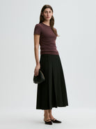 Woman wearing a purple shirt and black skirt holding a black handbag on a white background