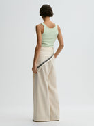 Woman wearing a light green sleeveless top and beige pants with lace trim on a white background