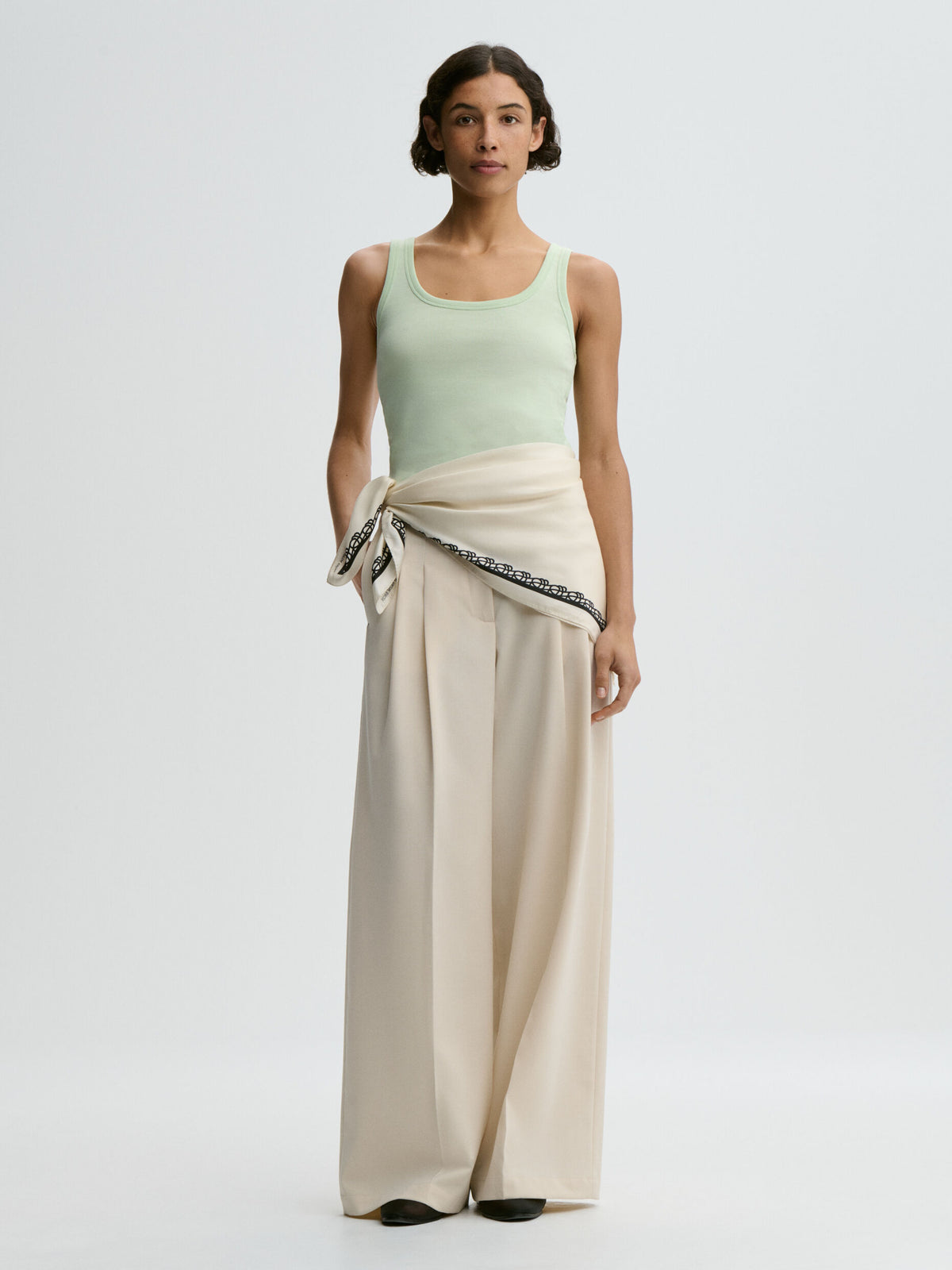 Woman wearing a light green sleeveless top and beige wide-leg pants on a white background