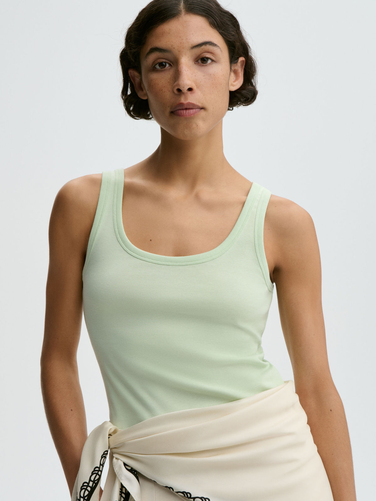 Woman wearing a light green tank top against a plain background