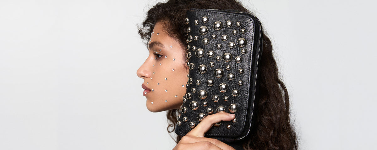 Woman holding a black studded clutch by Jerome Dreyfuss against a white background