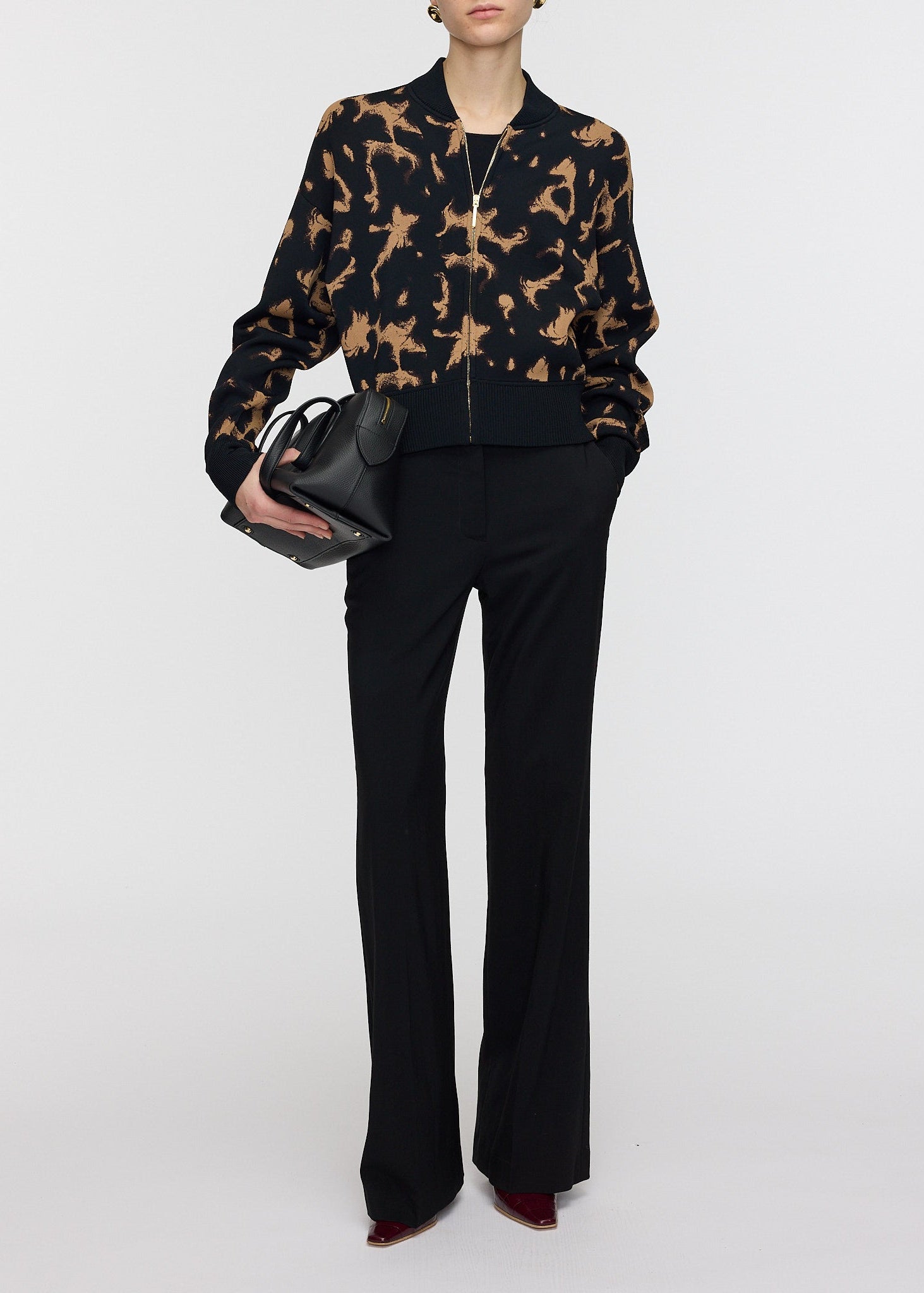 Person wearing a black and brown patterned jacket with black pants on a white background