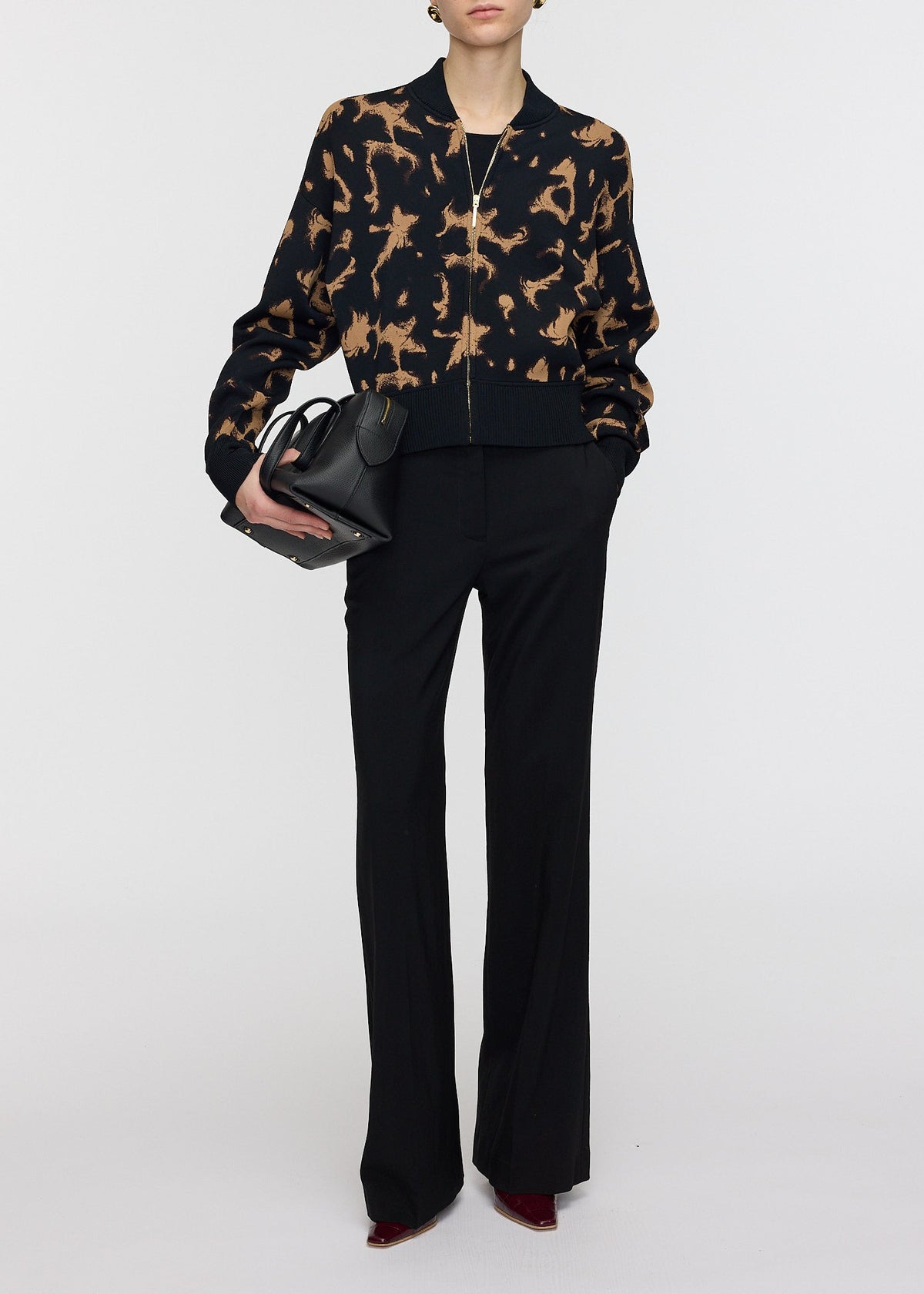 Person wearing a black and brown patterned jacket with black pants on a white background