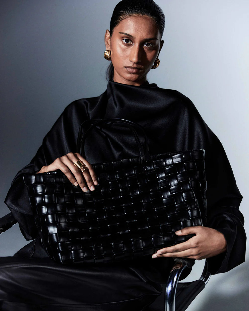 Woman holding a black woven handbag against a gray background