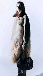 Person wearing a long coat with fur trim against a white background