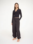 Woman wearing a black long-sleeve top and wide-leg pants on a white background