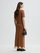 Woman wearing a brown dress with a sheer overlay on a white background