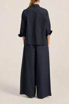 Person wearing a navy blue outfit with wide-leg pants on a beige background