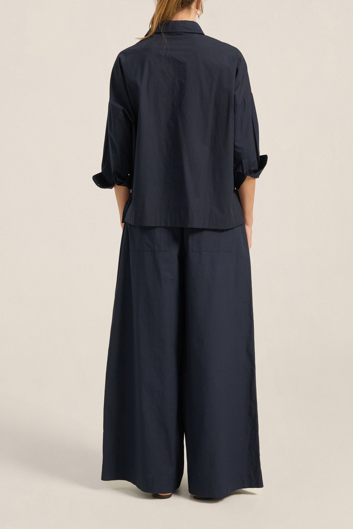 Person wearing a navy blue outfit with wide-leg pants on a beige background