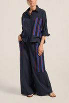 Woman wearing a navy shirt and wide-leg pants with red and blue stripes on a beige background