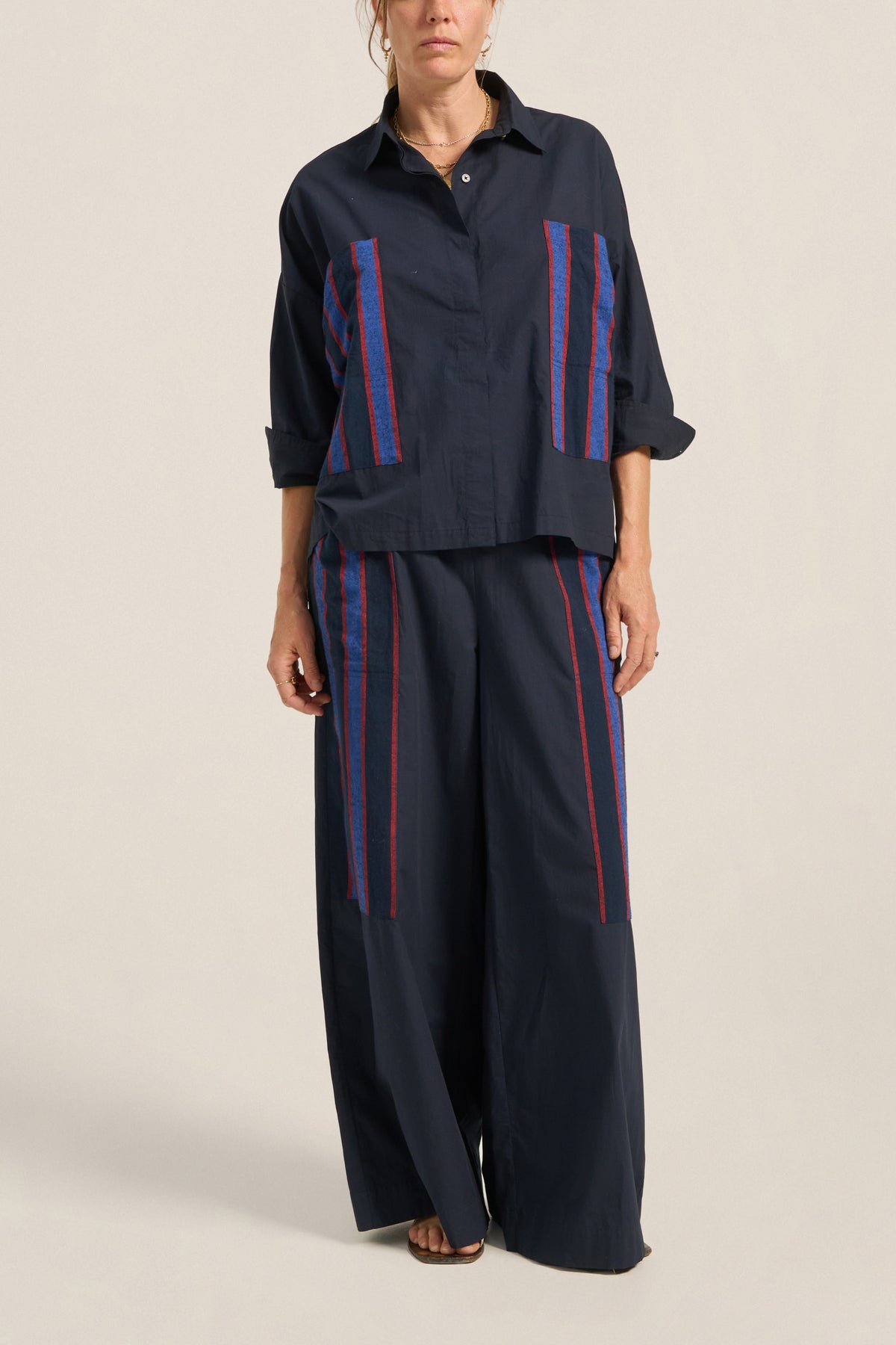 Person wearing a navy outfit with red and blue stripes on a beige background