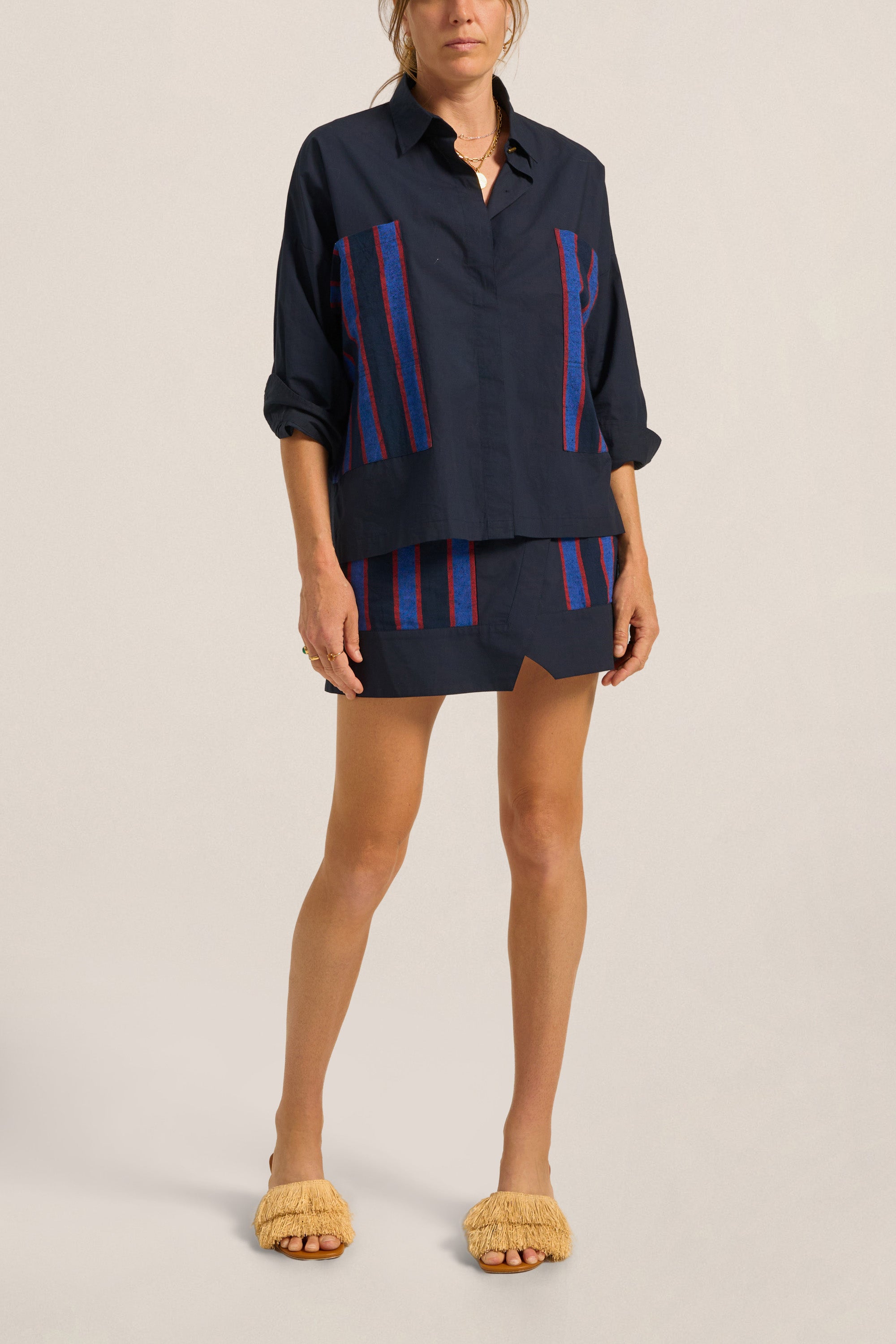 Woman wearing a navy outfit with red and blue striped accents on a beige background