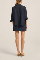 Person wearing a navy blue outfit with a jacket and skirt on a beige background