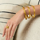 Gold bracelets and ring on a person's wrist against a neutral background