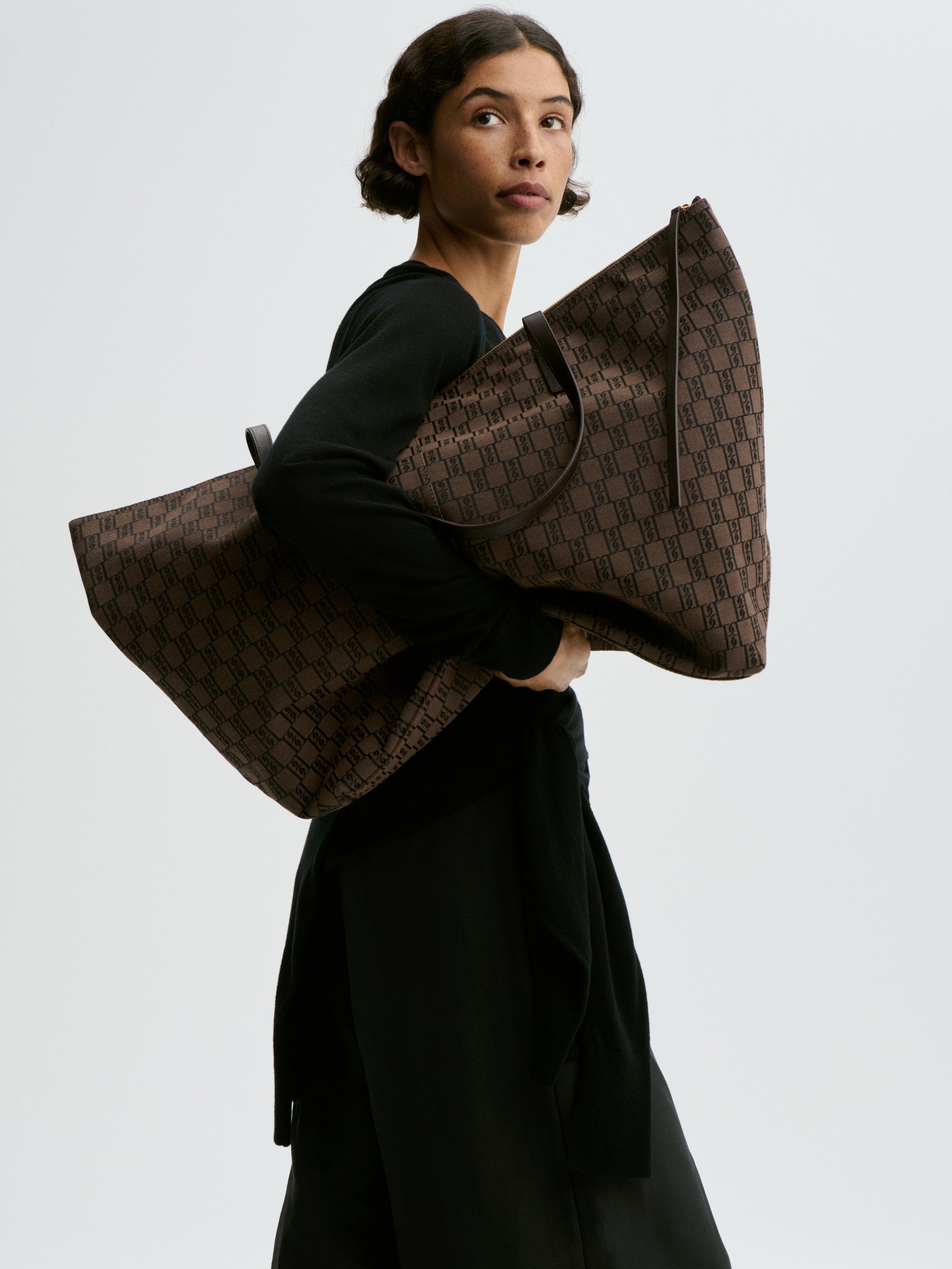 Person holding a large brown patterned bag against a plain background
