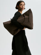 Person holding a large brown patterned bag against a plain background