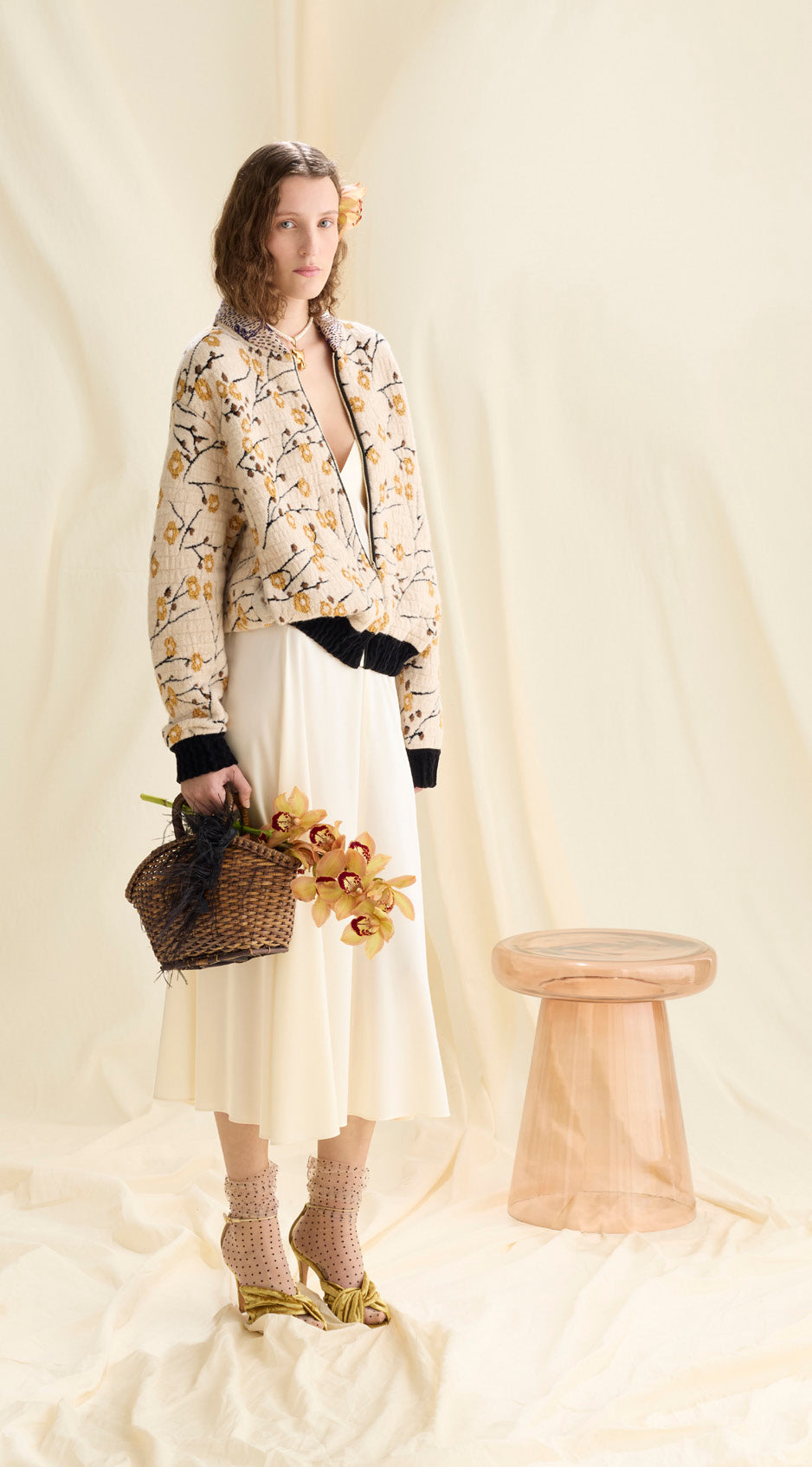 Woman in a floral jacket and white skirt holding flowers against a plain background