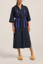 Woman wearing a navy dress with red and blue striped accents on a plain background