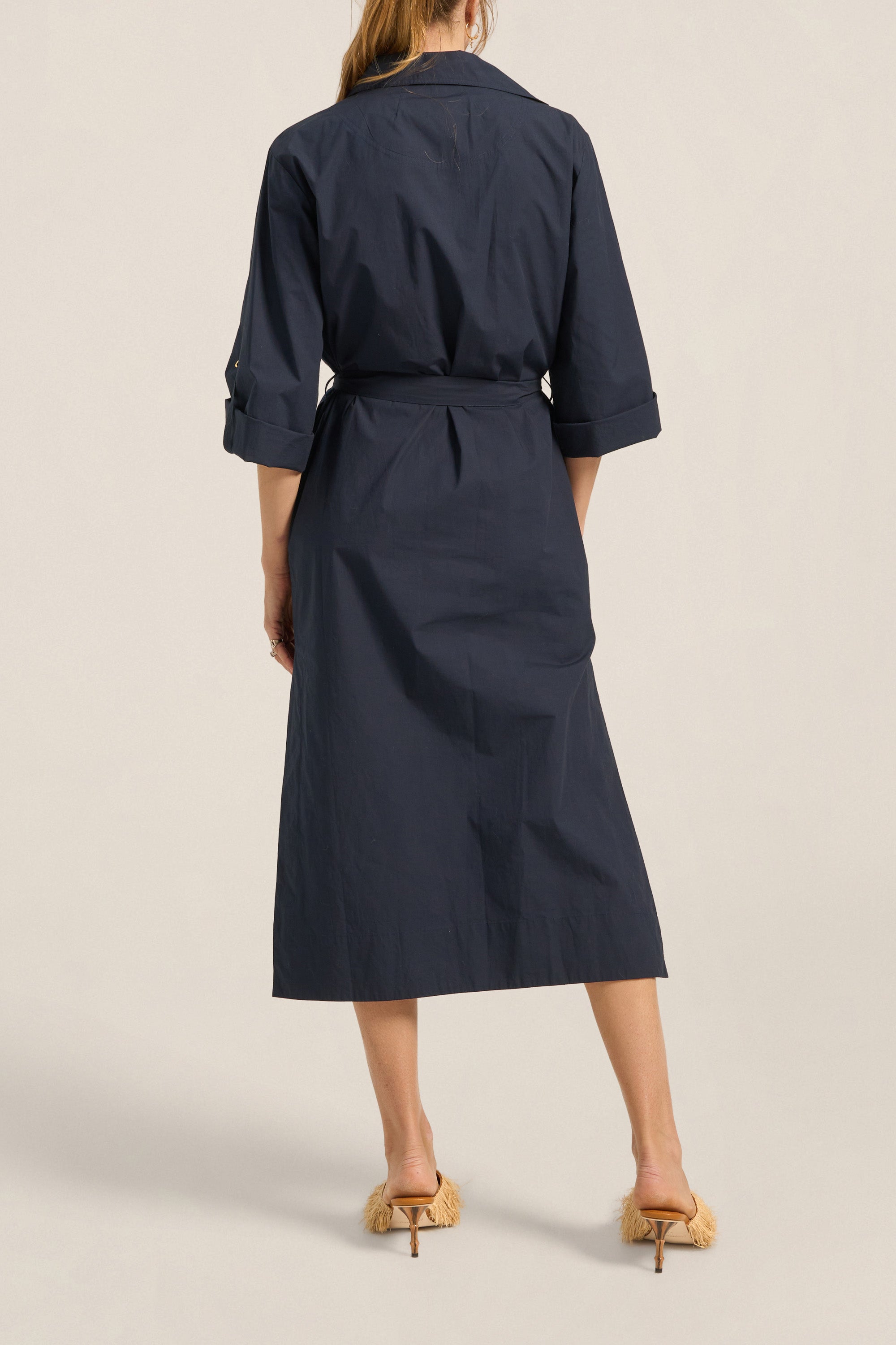 Navy trench coat worn by a person on a beige background