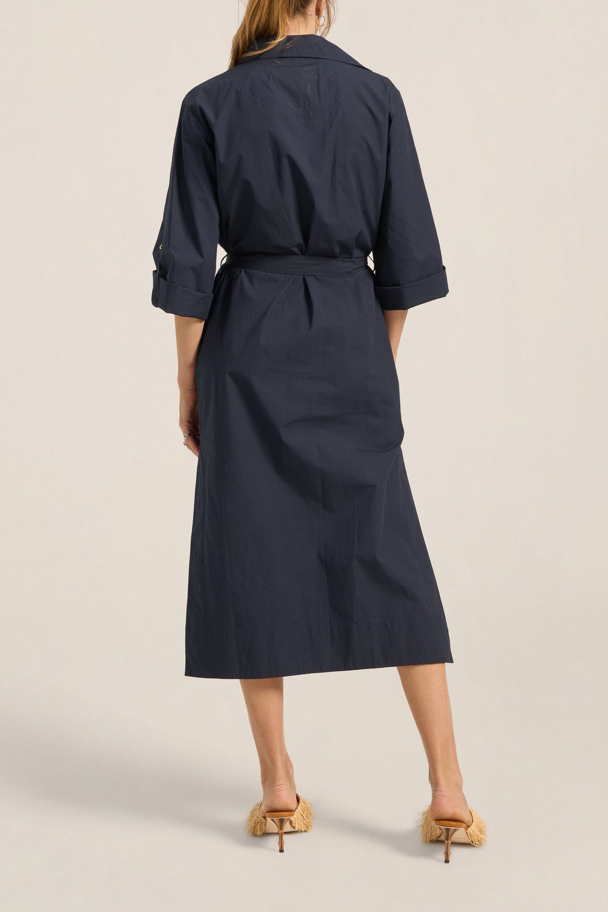 Navy trench coat worn by a person on a beige background