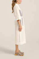 Woman wearing a white dress with a gray pattern on a plain background
