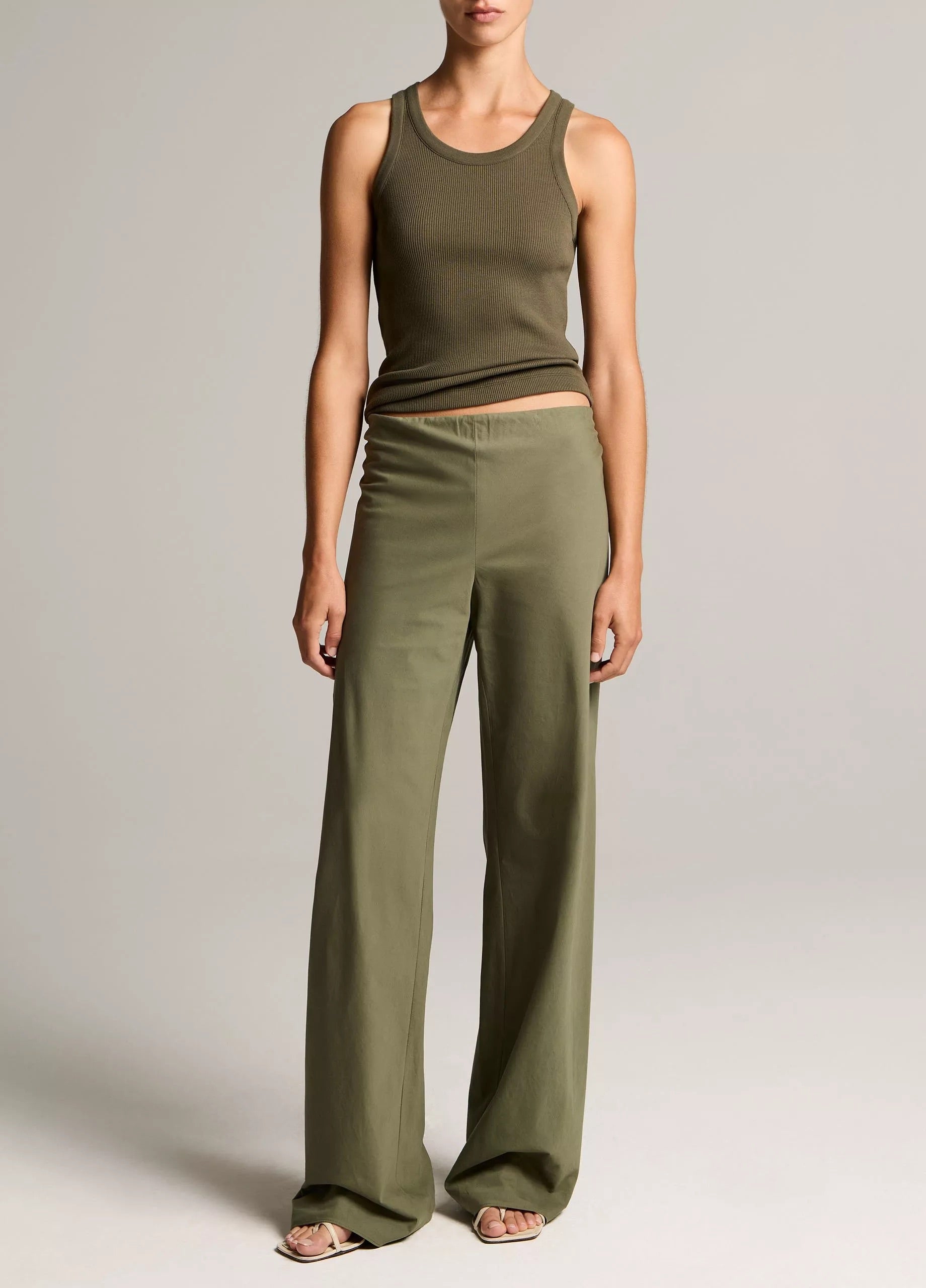 Person wearing an olive green tank top and wide-leg pants on a plain background