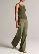 Person wearing an olive green tank top and wide-leg pants on a plain background
