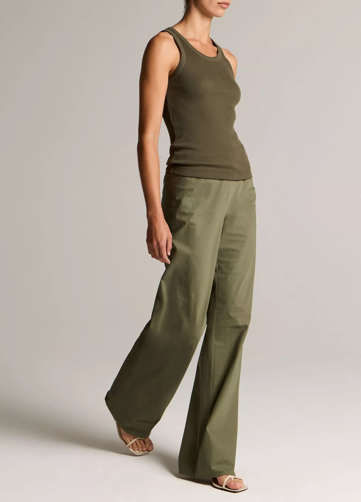 Person wearing an olive green tank top and wide-leg pants on a plain background