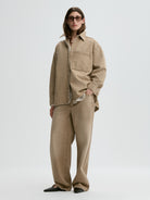Person wearing a beige jacket and pants on a white background