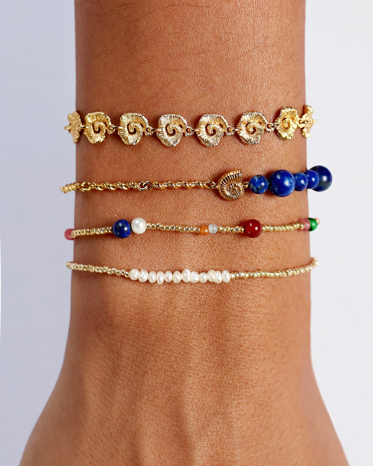 Multiple bracelets on a wrist against a neutral background