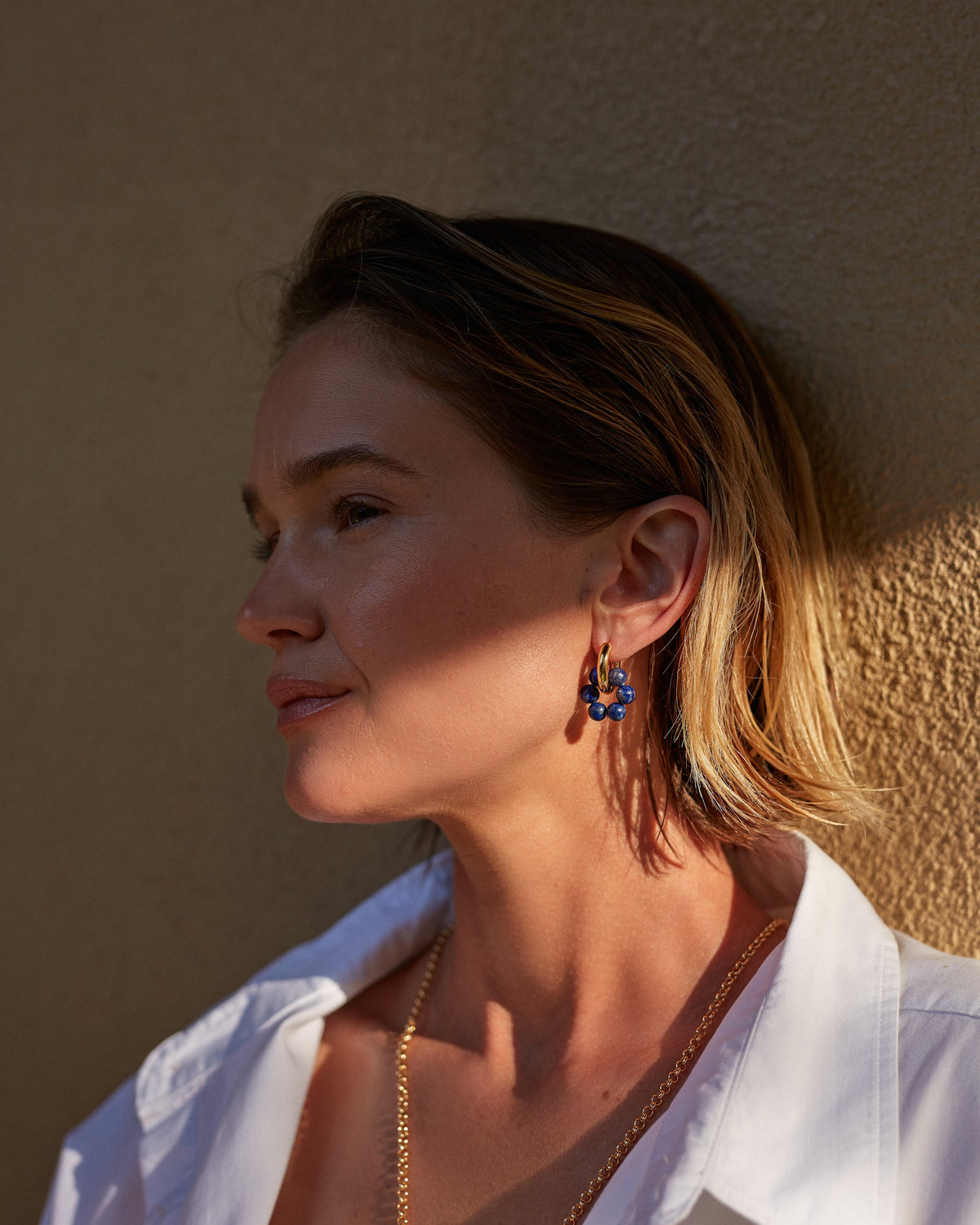 Woman wearing a white shirt and earrings against a beige wall