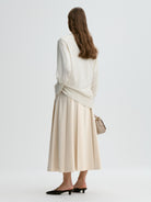 Woman wearing a white top and beige skirt with a handbag on a light gray background