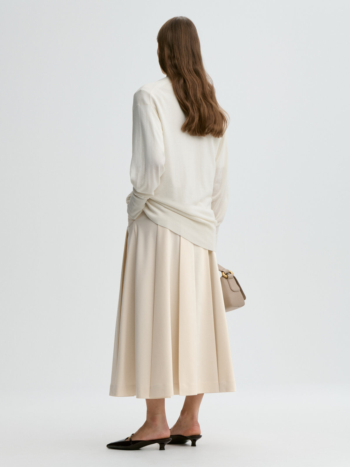 Woman wearing a white top and beige skirt with a handbag on a light gray background
