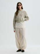 Person wearing a patterned sweater and beige pants on a white background