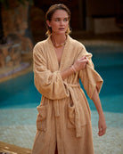 Woman in a beige robe standing by a poolside