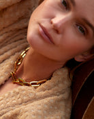 Close-up of a person wearing a gold chain necklace with a soft, neutral background.