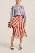 Woman wearing a blue embroidered blouse and red and white striped skirt on a beige background