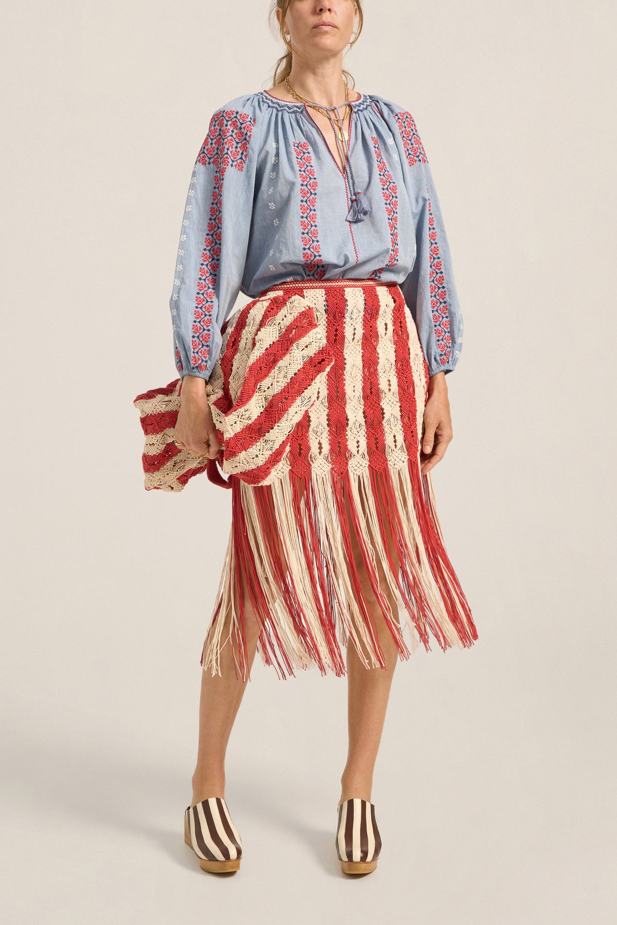 Woman wearing a blue embroidered blouse and red and white striped skirt on a beige background