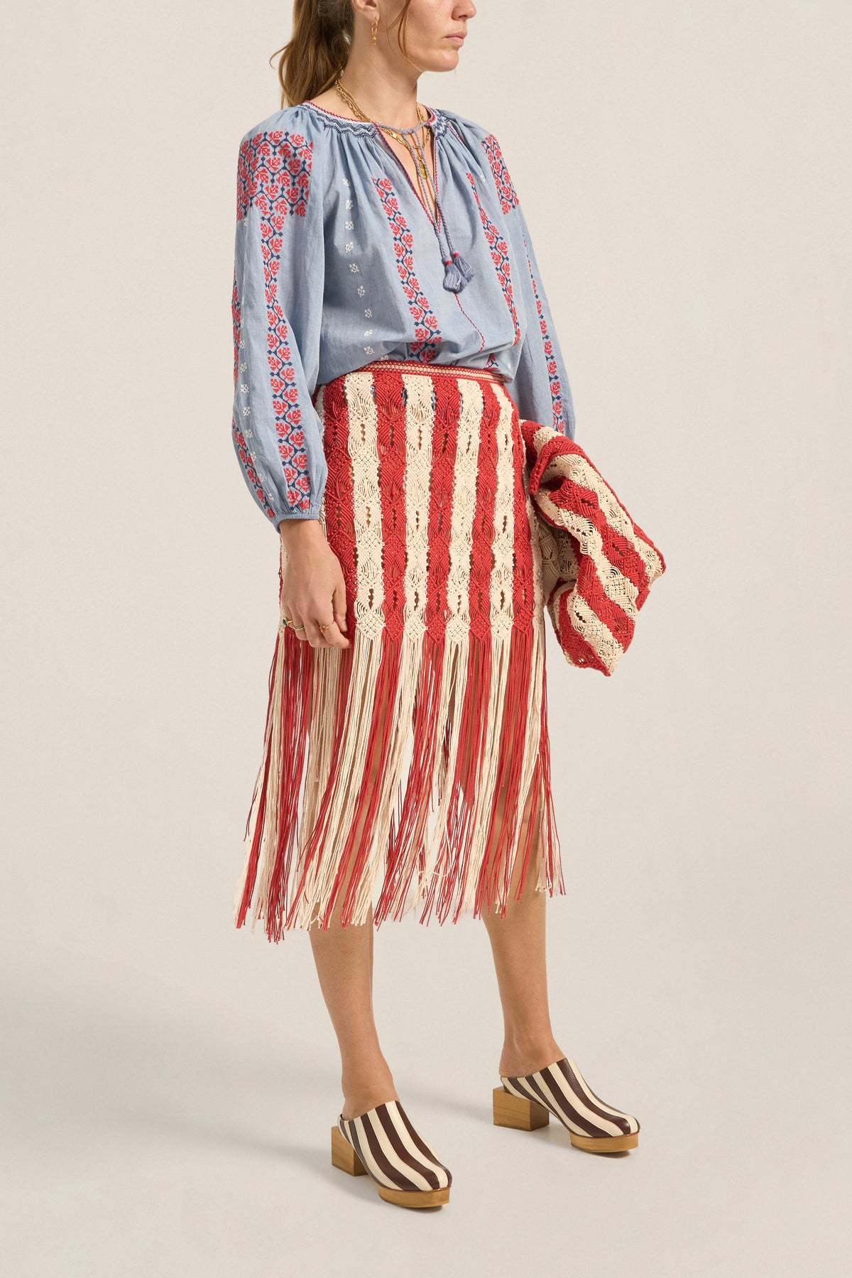 Woman wearing a blue embroidered blouse and red and white striped skirt on a beige background
