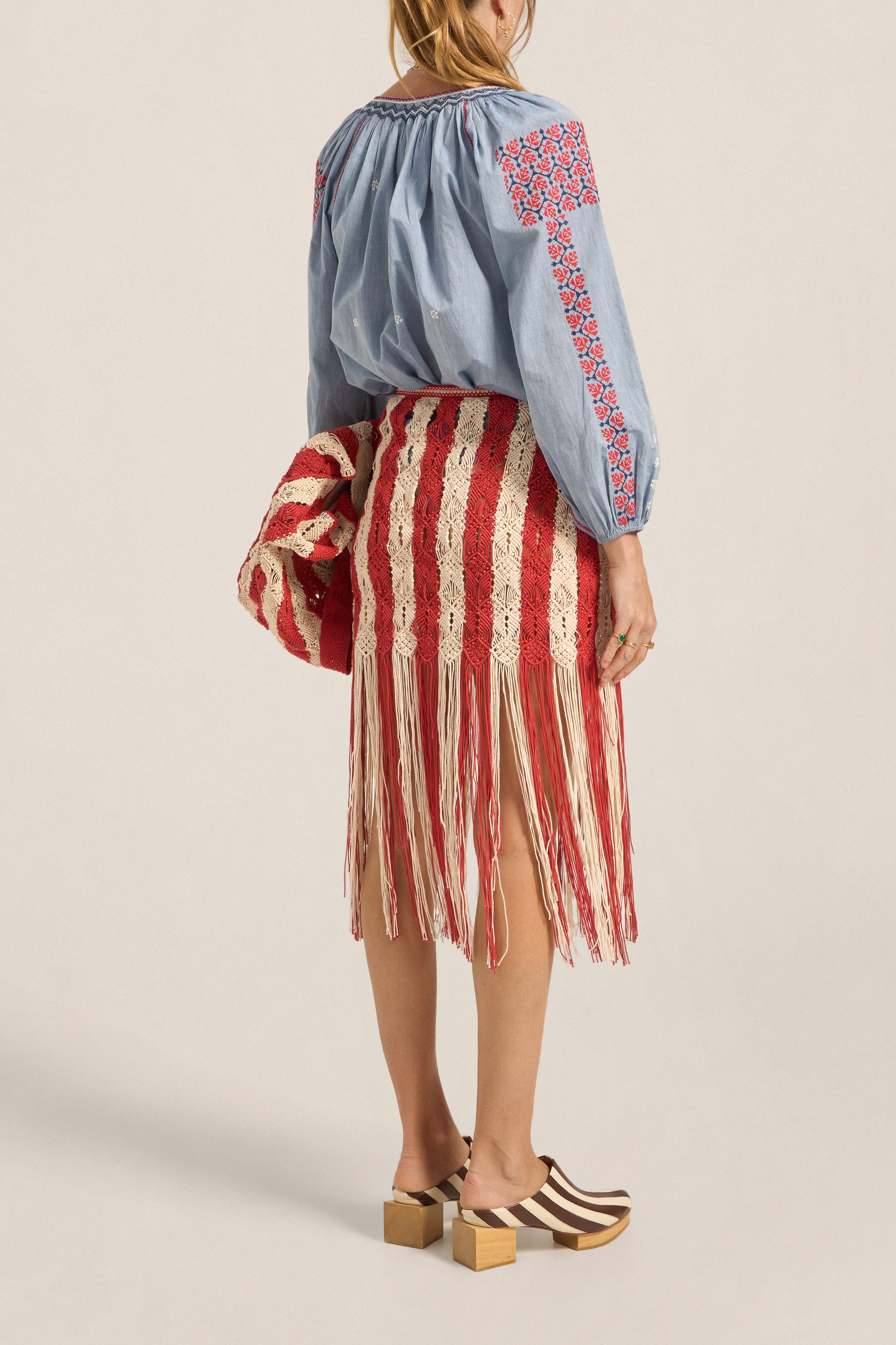 Woman wearing a blue blouse with red and white embroidery and a red and white striped skirt on a beige background