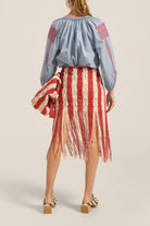 Woman wearing a blue embroidered blouse and red and white striped skirt on a beige background