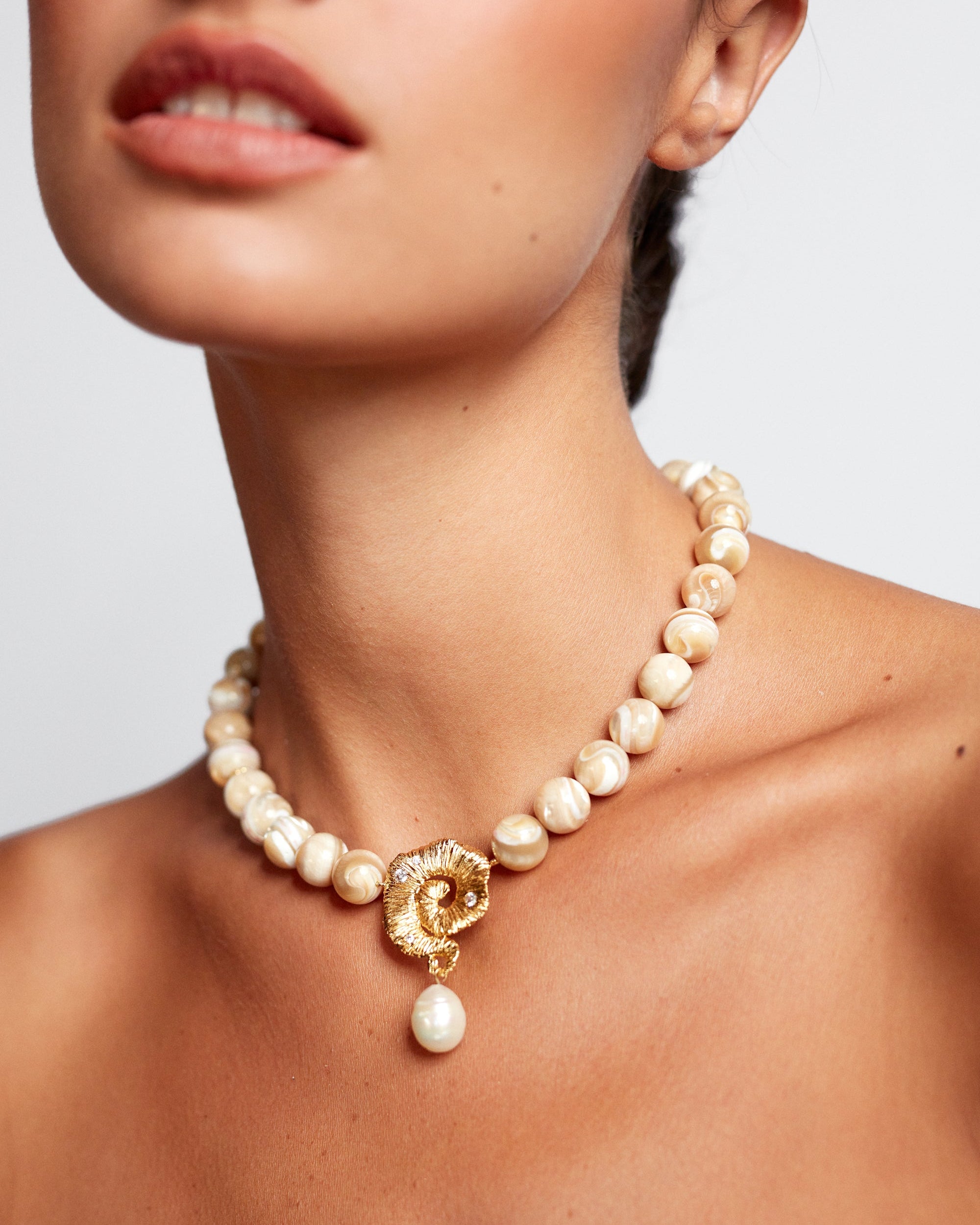 Pearl necklace with a gold clasp worn by a model on a neutral background