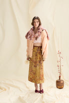Woman wearing a floral outfit with a pink jacket and yellow skirt, standing against a white background.