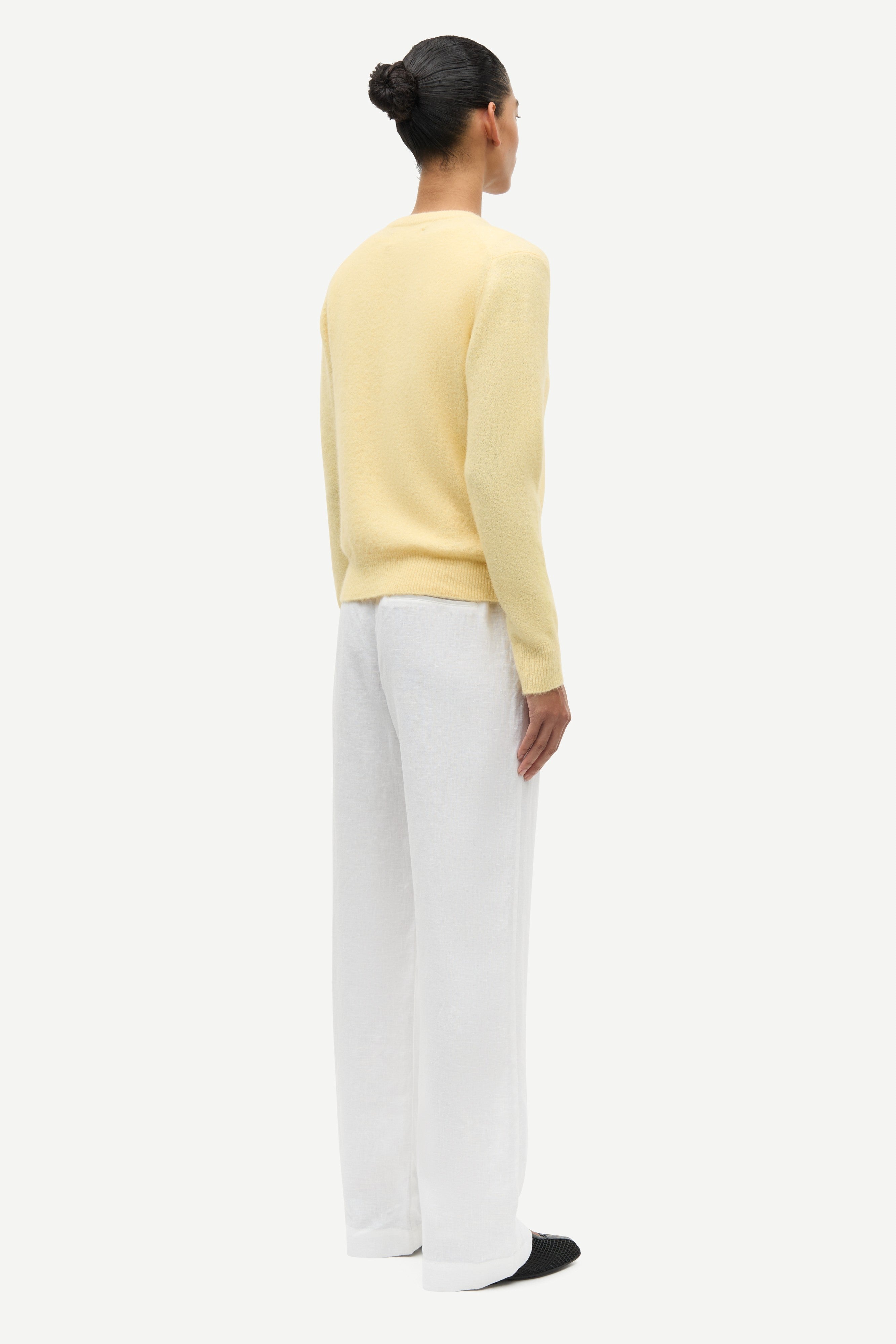 Person wearing a yellow sweater and white pants on a white background