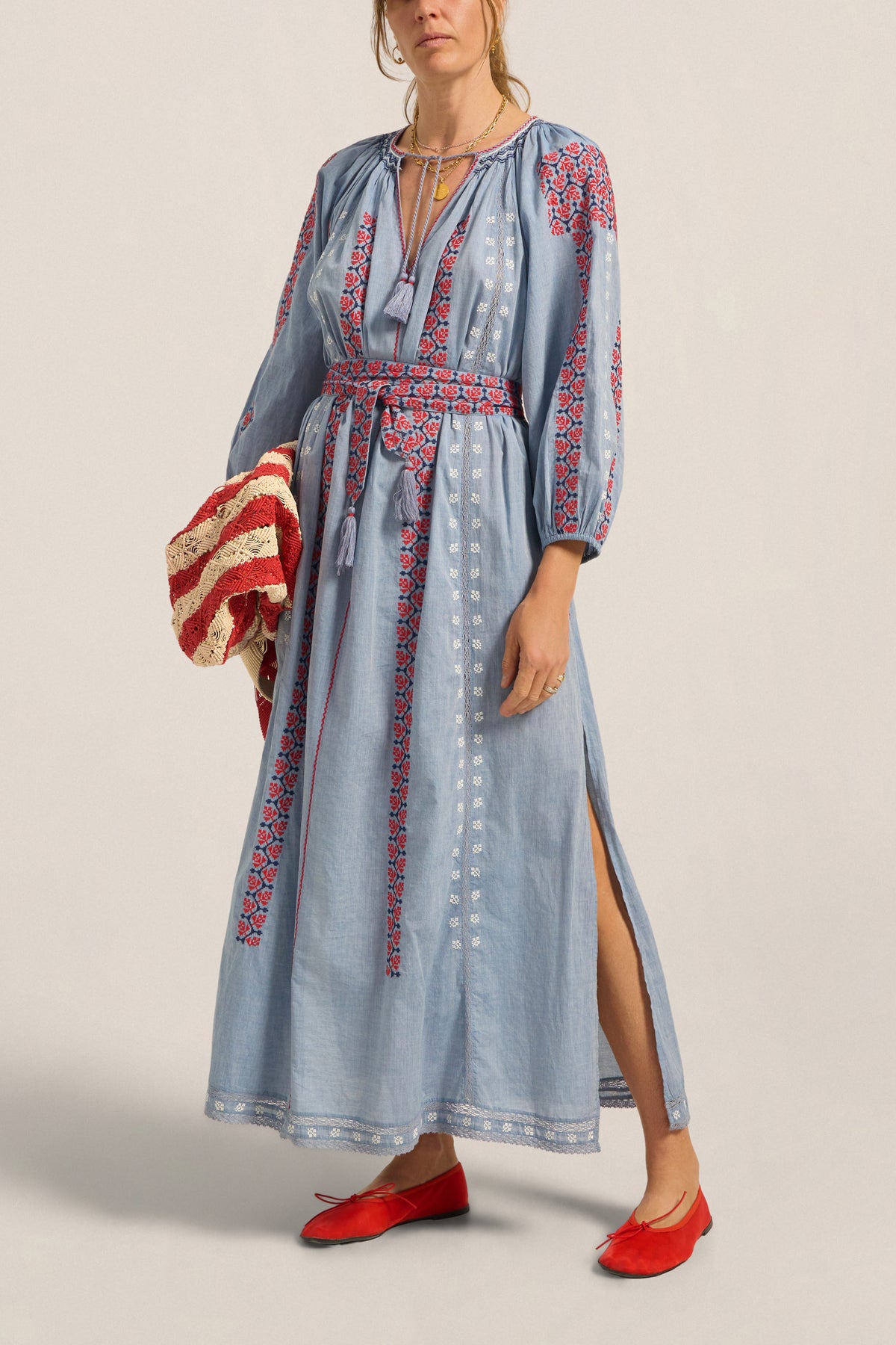 Woman wearing a long blue dress with red and white patterns on a beige background